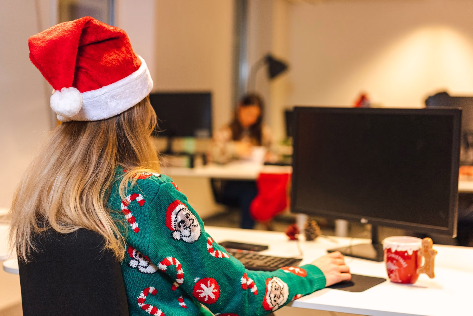 a woman wearing christmas sweater sitting in front of a computer